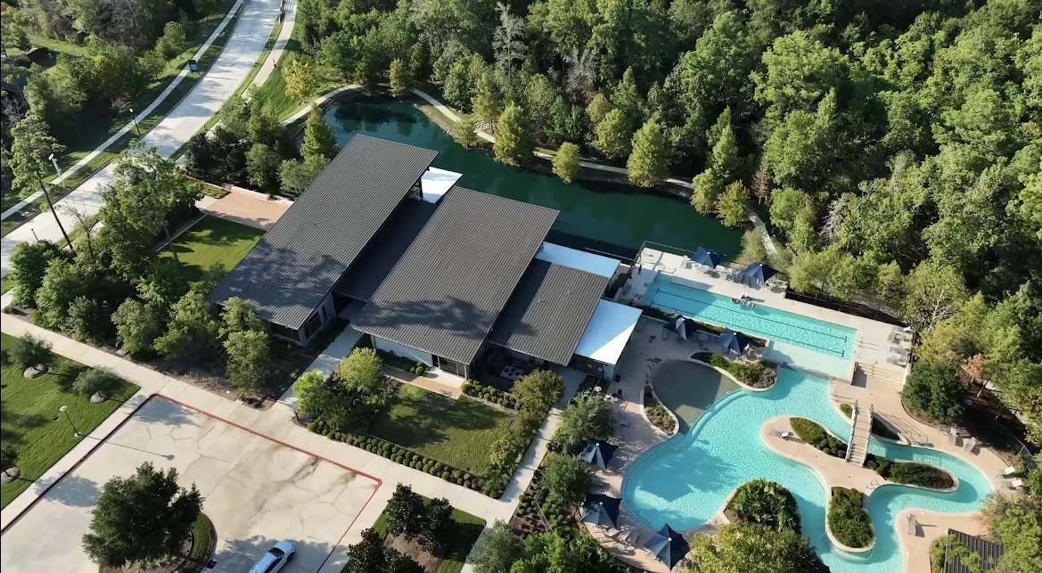 Aerial view of a neighborhood pool and clubhouse surrounded by pines